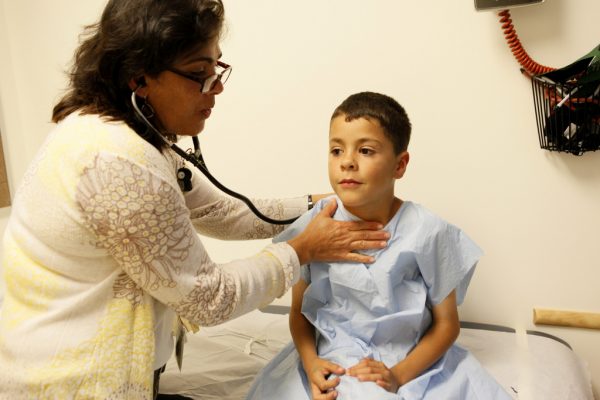 clinician with stethoscope examining a young boy