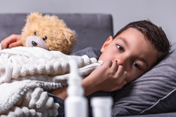 Child sick, in bed, holding a teddy bear.